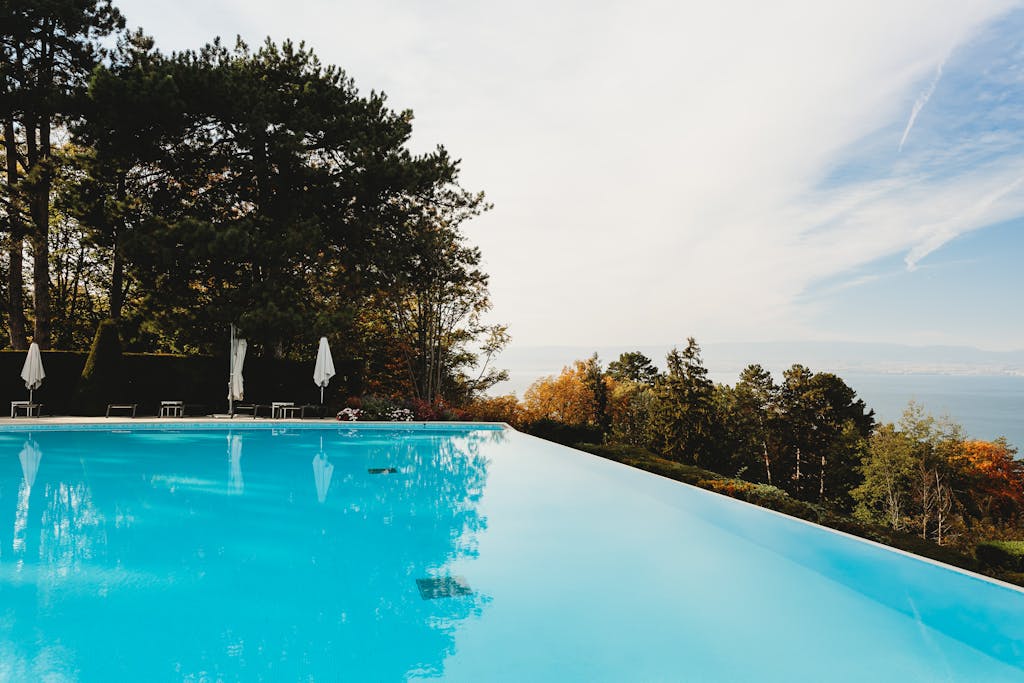 Infinity pool with umbrella-shaded loungers overlooking a lush forest, perfect for relaxation.